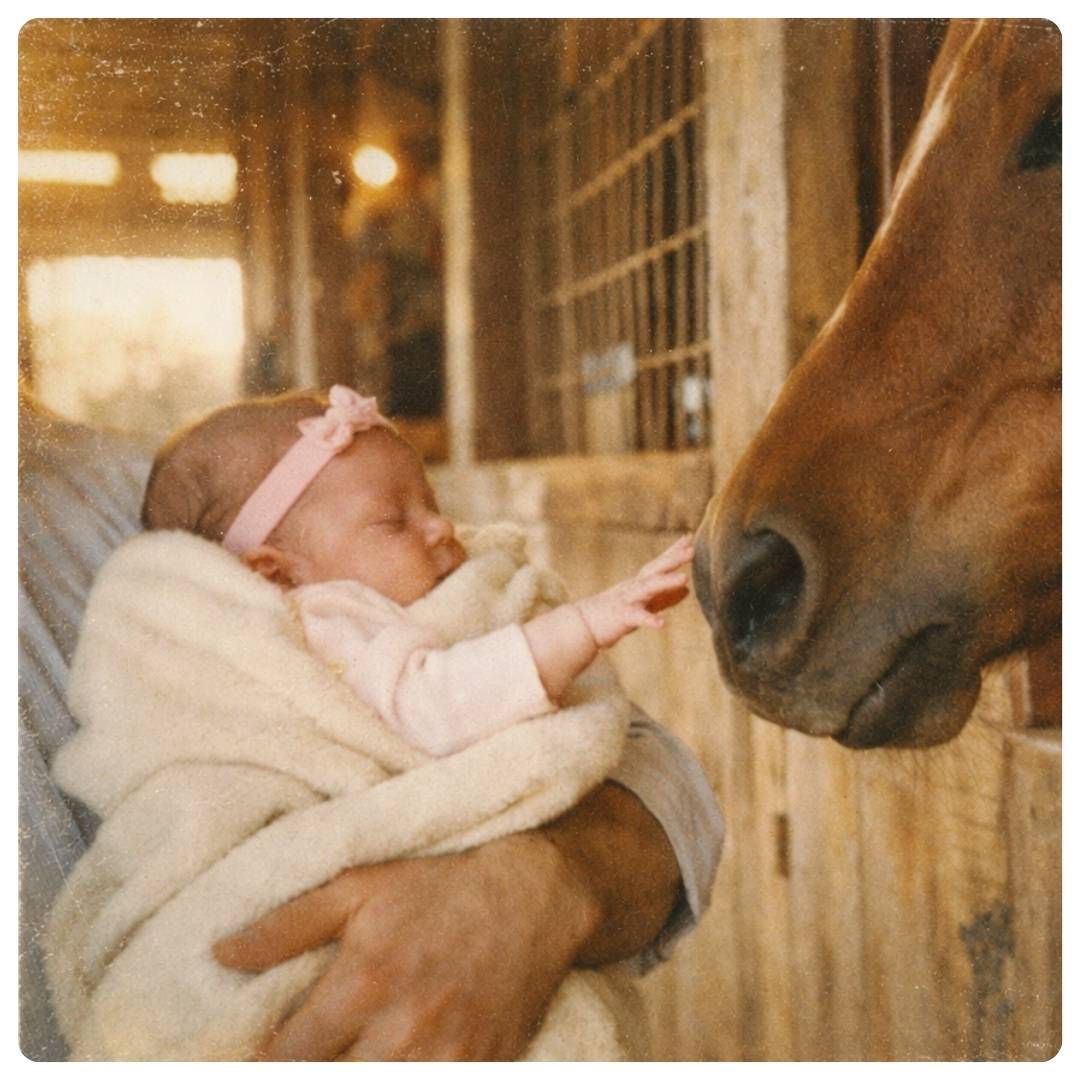 Newborn baby being held close to a horse in a barn setting
